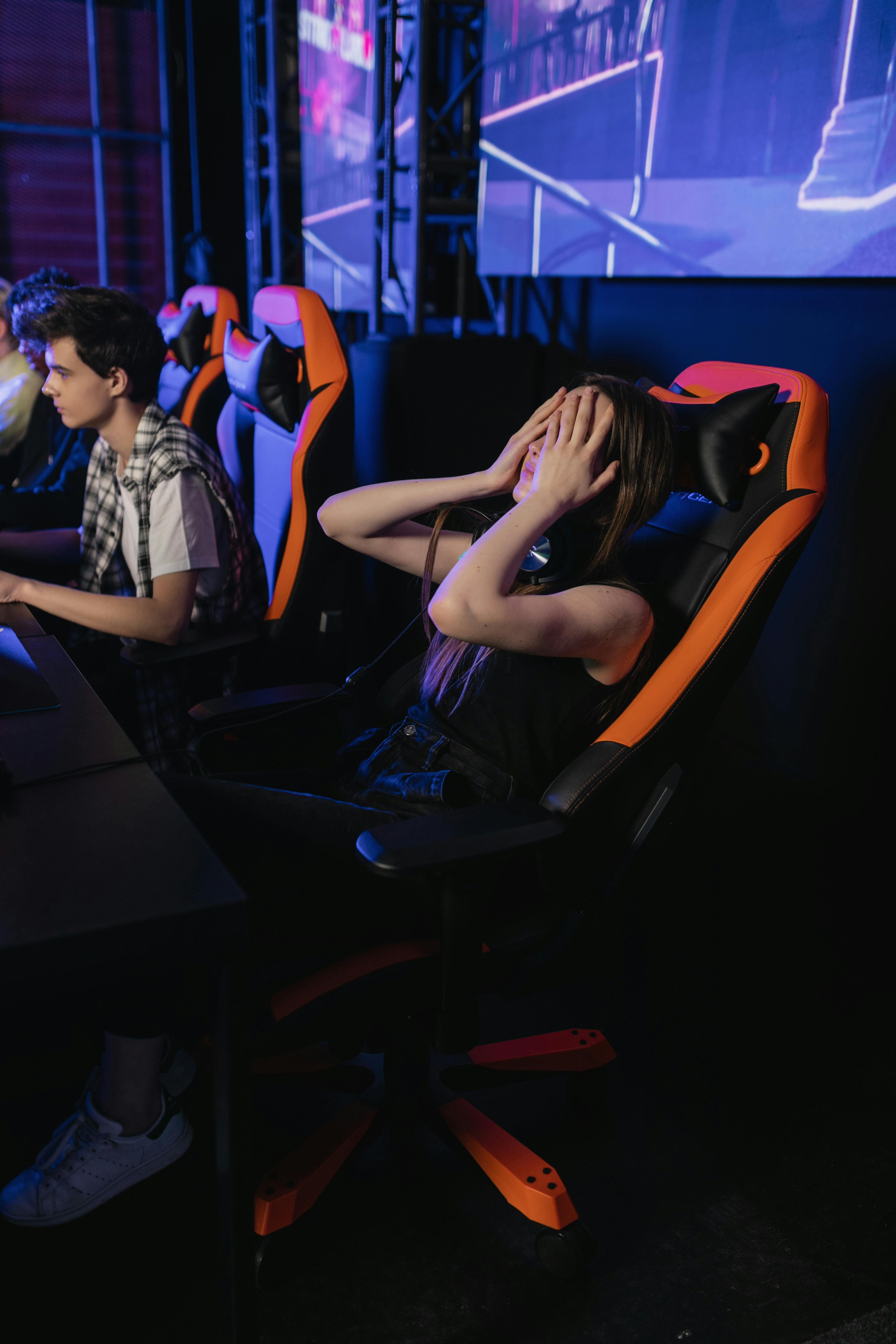 Woman covering eyes in gaming chair at esports event, expressing frustration after a loss.