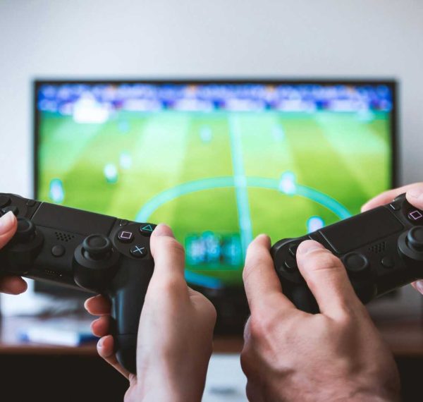 Close-up of hands holding gaming controllers in front of a TV. Engaged in a video gaming session.