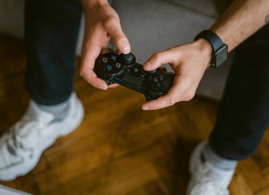 A person holding a gaming controller indoors, wearing casual attire with a smartwatch.