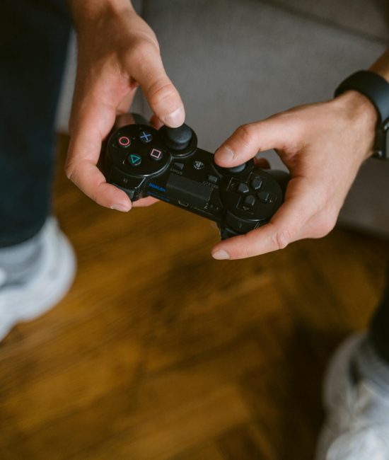 A person holding a gaming controller indoors, wearing casual attire with a smartwatch.