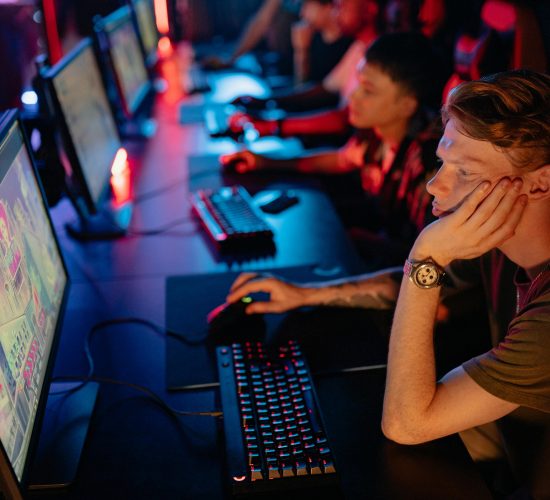 Gamers intensely focused on a computer game during an online esport competition in a dimly lit arena.